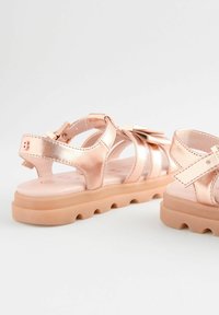 Roze gouden metallic sandalen met uitgesneden ontwerp, voorzien van een strikaccent en een lichtbeige, gestructureerde zool. Zachte voering is zichtbaar.