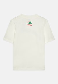 Rövid ujjú krémszínű póló, hátul grafikus mintával, zöld geometriai alakzatokkal és piros kockás mintával az alján.