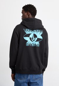 Sort hættebluse med et stort lyseblåt grafisk design med "VOLCOM" og "STONE" tekst på ryggen. Blødt stof med en afslappet pasform.