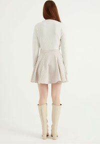 Béžová sukně s houndstooth vzorem a zvonovým střihem, spárovaná s světle šedým žebrovaným svetrem a béžovými vysokými botami až ke kolenům. Hladká textura po celém povrchu.