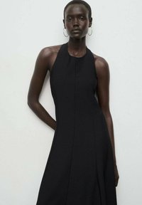 Vestido negro sin mangas con cuello halter, de textura suave, con cuerpo entallado y falda acampanada. Presenta un diseño minimalista y líneas limpias.