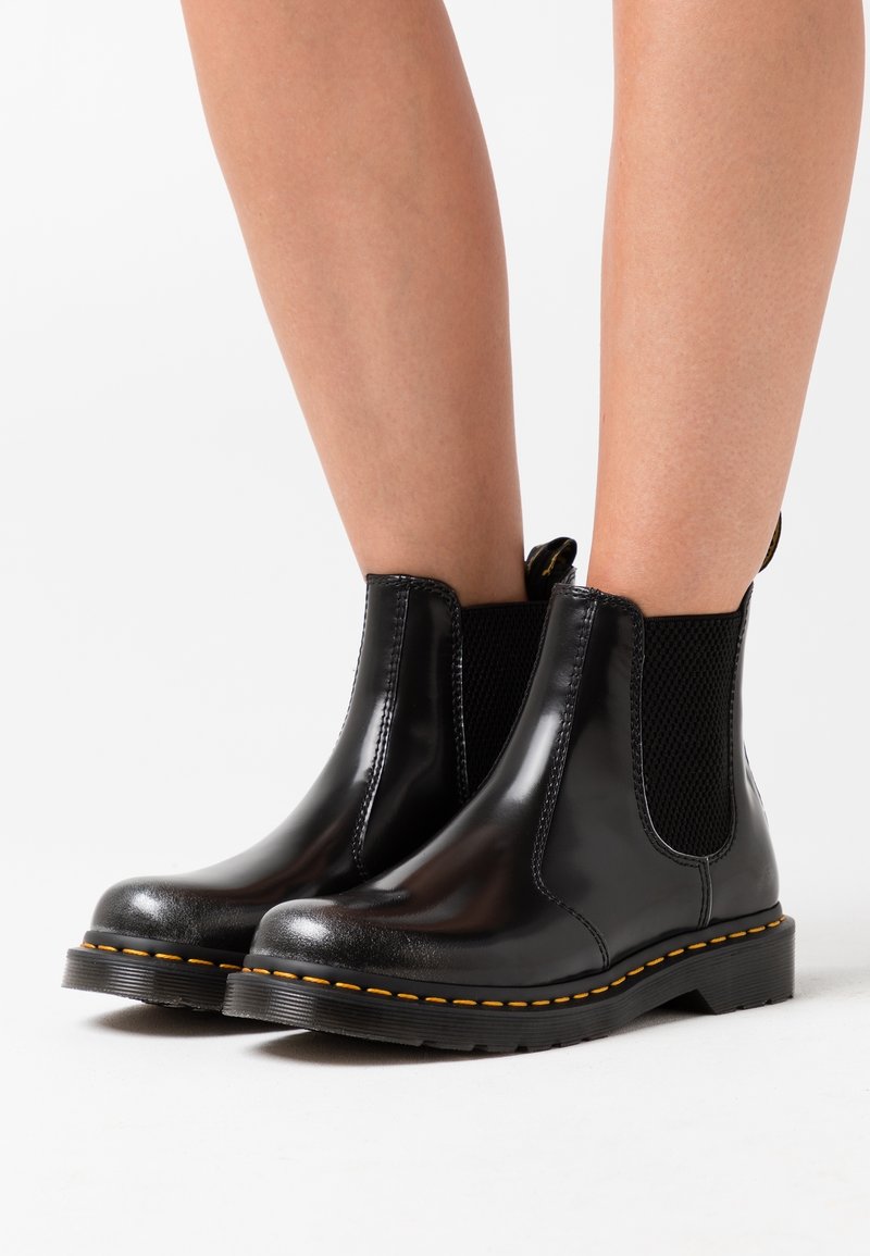 Bottines en cuir noir avec panneaux élastiques sur les côtés, surpiqûres jaunes, bout rond et semelle texturée. Onglet de tirage contrasté à l'arrière.