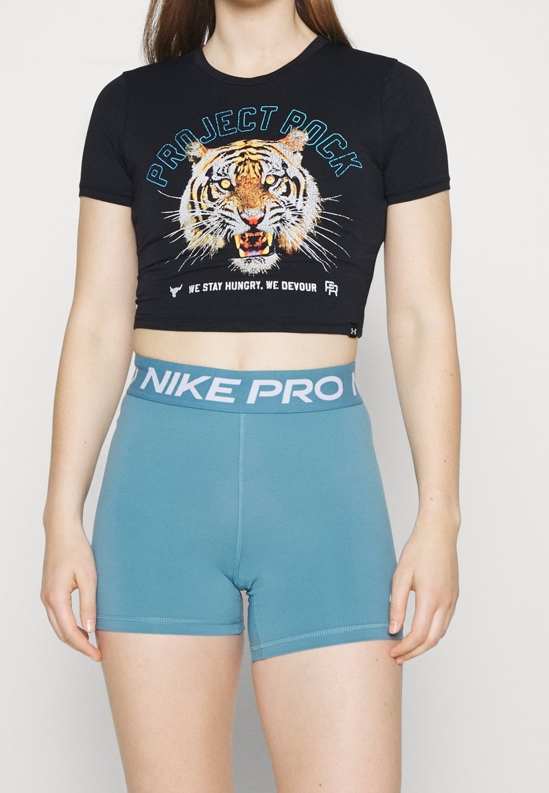 Kvinna iklädd en svart kort t-shirt med en tiger grafik och text, som matchar med högmidjade blå Nike Pro träningsshorts.