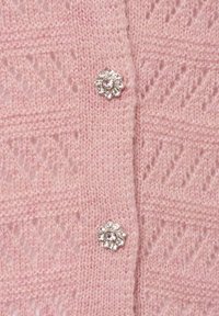 Helle rosa gestrickte Cardigan mit einem Zickzackmuster, ausgestattet mit zwei dekorativen Blumenknöpfen, die mit klaren Steinen verziert sind.