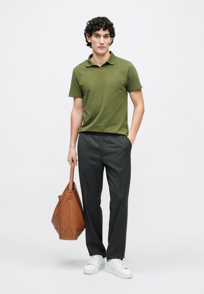 Zaļš īsroku polo krekls, pelēkas bikses un baltas sporta kurpes. Brūna ādas soma ar strukturētu dizainu. Kopumā gluda tekstūra.