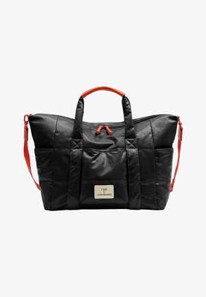 Sac de voyage matelassé noir avec poignées et fermetures éclair rouges, poche avant avec étiquette blanche, et bandoulière rouge détachable.