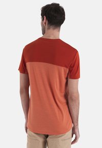 T-shirt a maniche corte in sfumature di ruggine e arancione, con scollo rotondo e texture liscia. Nessun motivo o dettaglio visibile.