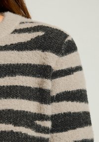 Strikket sweater i beige med sorte vandrette striber. Blød, fuzzy tekstur med udtalt striber. Rund hals og afslappet pasform.
