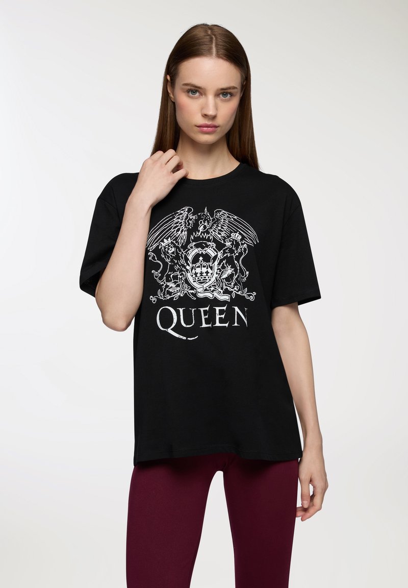 T-shirt in cotone nero con un design grafico bianco che raffigura una corona, leoni e ali con la parola "QUEEN" in basso.