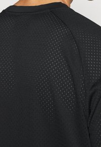 Svart kortärmad topp i andningsbart meshmaterial med ett perforerat mönster. Har rund halsringning och raglanärmar.