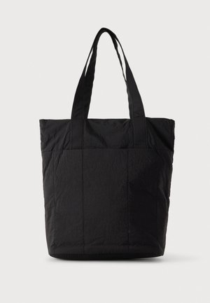 Sac cabas en tissu noir avec deux longues anses d’épaule, une large ouverture sur le dessus et des panneaux avant cousus.
