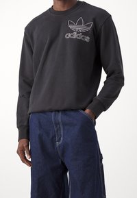 Černá mikina z bavlny s kulatým výstřihem a žebrovanými manžetami; na hrudi se nachází vyšívané bílé logo Adidas.