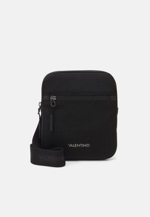 Sac bandoulière en nylon noir avec une surface lisse, comportant une poche zippée à l'avant, une bandoulière réglable et le logo "Valentino" en argent.