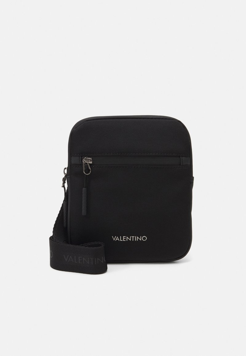 Sac bandoulière en nylon noir avec une surface lisse, comportant une poche zippée à l'avant, une bandoulière réglable et le logo "Valentino" en argent.