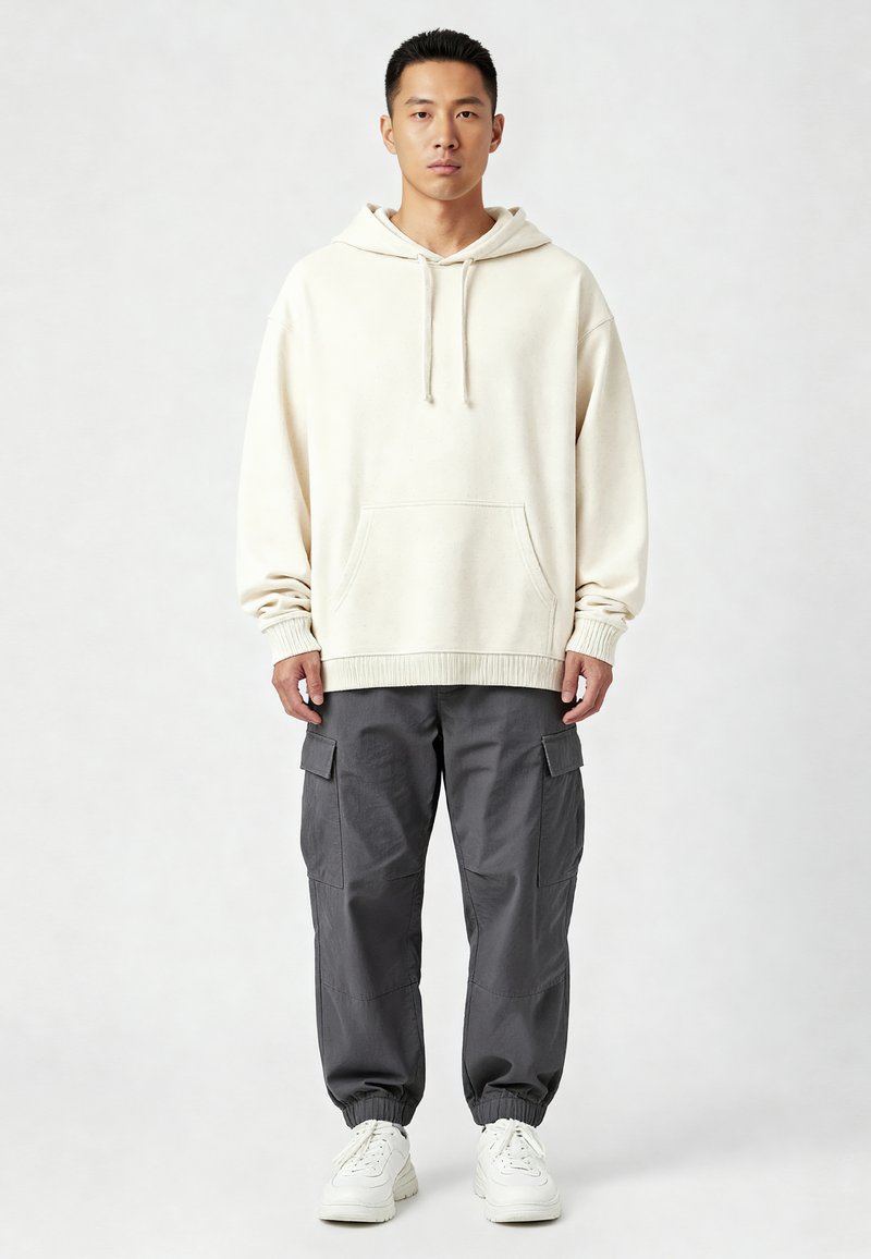 Krém színű kapucnis pulóver, elülső zsebbel és húzózsinórral, sötétszürke cargo nadrággal párosítva, oldalzsebekkel. Fehér sportcipők teljesítik a megjelenést.