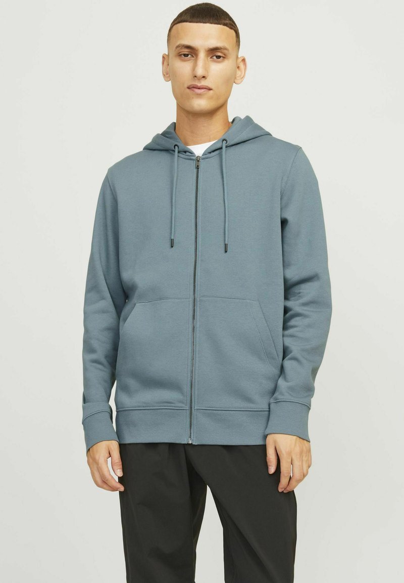 Felpa con zip azzurro chiaro in morbido cotone misto, dotata di cappuccio con cordino, tasche frontali e polsini a coste, abbinata a pantaloni scuri.