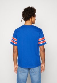 Camiseta de algodón azul con mangas cortas que presenta rayas horizontales rojas y blancas. Cuello redondo con un dobladillo recto, combinada con jeans azules.