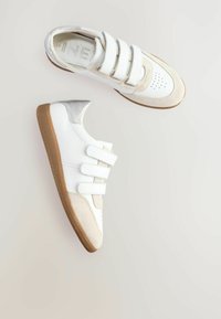 Białe sneakersy z trzema paskami na rzep, wykonane z skóry i zamszu, z zaokrąglonym noskiem, kontrastowymi beżowymi akcentami i gumową podeszwą.