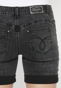 Črne denim kratke hlače z zavitimi robovi, ki imajo gladko teksturo, dve zadnji žepu in dekorativne šive v obliki zanke.