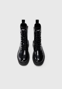 Stivaletti alla caviglia in pelle verniciata nera con lacci frontali, zip laterale e dettagli studded lungo la suola. Design pulito e moderno.
