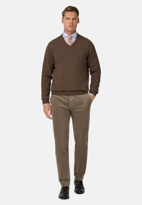 Maglione marrone a scollo a V in un morbido tessuto a maglia abbinato a pantaloni di velluto a costine marrone chiaro. L'outfit è completato da scarpe eleganti nere.