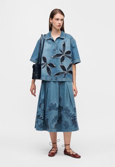 Tenue en denim comprenant un haut à manches courtes avec broderies florales et une jupe midi assortie, toutes deux dans des tons bleus, complétées par des chaussures marron à lacets.