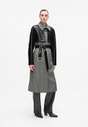 Grey wool-blend trench coat with black leather sleeves, a large collar, belted waist, and a sleek, structured design.