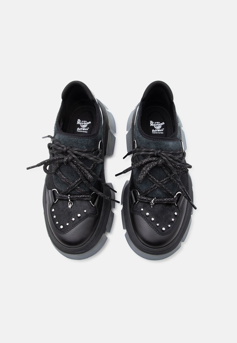 Schwarze klobige Plateau-Schuhe mit Stern- und Nietenverzierung an der Spitze, dicken gesprenkelten Schnürsenkeln und gebrandeten Innensohlen vor weißem Hintergrund.