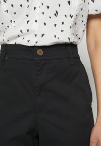 Pantaloni neri in cotone con una texture liscia, dotati di chiusura frontale con bottone, tasche laterali e vita aderente.