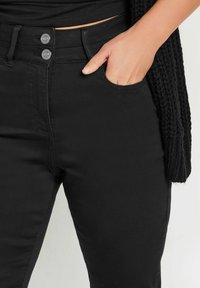 Svarta denimjeans med hög midja, två framknappar och en framficka. Slät yta och robusta sömdetaljer.