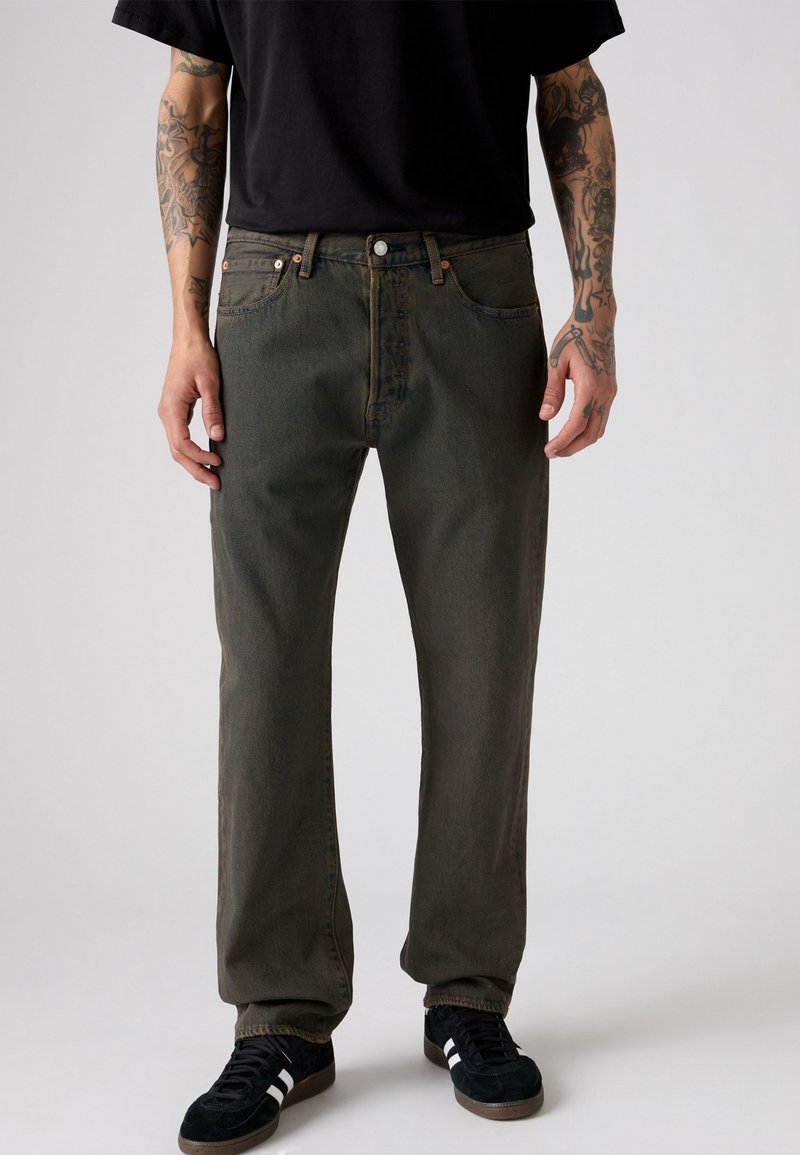 Donkergroene denim spijkerbroek met een rechte pasvorm, vijf-pocket ontwerp en contrasterende stiksels, gecombineerd met zwarte sneakers en een zwart t-shirt.