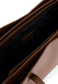 Brown leather handbag with a smooth exterior, gold zipper, and black lined interior featuring a repeating logo pattern. Two compartment design.