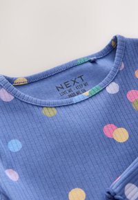 Camiseta azul de canalé con lunares multicolores y escote redondo, con etiqueta impresa con el nombre de la marca "NEXT" e instrucciones de cuidado.