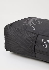 Sac à dos de sport noir avec un panneau latéral texturé, logo PUMA et matériau lisse. Il dispose d'une fermeture éclair et d'une forme rectangulaire.