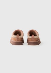 Pair of tan slip-on shoes with textured cream collar and brown rubber soles, viewed from the back on a white background.