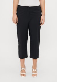 Black cropped trousers with a smooth texture, featuring a button closure and a straight cut. Worn with white strappy sandals.