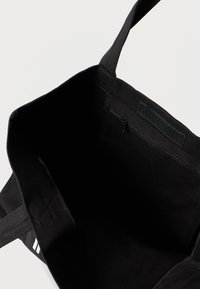 Melna audekla iepirkumu soma ar divām izturīgām siksnām, iekšpusē ar rāvējslēdzēja kabatu un gludu odere. Minimālistisks dizains, bez ārējām rotājumiem.