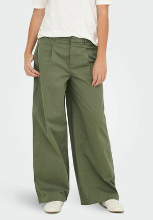 Pantalons larges en coton vert olive, avec un pli avant, des poches latérales et une taille mi-haute, associés à des baskets blanches.