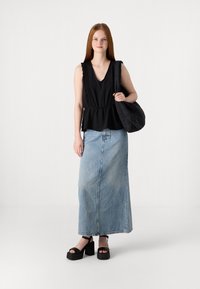 Svart ermeløs topp med v-hals og blonder, kombinert med en denim maxiskjørt. Sorte plattform sandaler og en quilted svart veske aksenterer stilen.
