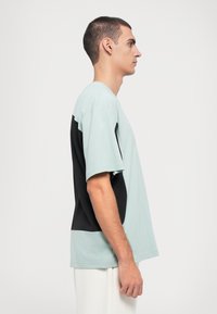 Μίντι πράσ�ινη και μαύρη κοντομάνικη μπλούζα με στρογγυλή λαιμόκοψη, διαθέτοντας αντίθετους χρωματισμούς και χαλαρή γραμμή. Μαλακό βαμβακερό υλικό.