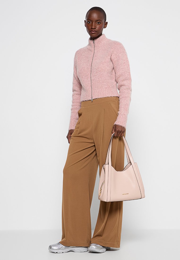 Lichtroze, ritssluiting, cropped trui; beige, wijde broek; zachte roze handtas met twee handvatten; zilveren sportschoenen; minimale achtergrond.