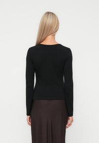 Haut noir à manches longues en matière lisse, avec un col rond et une silhouette ajustée, associé à une jupe marron.