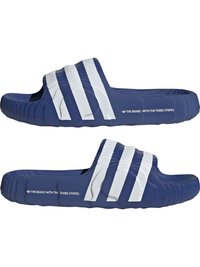 Temno modre natikače iz teksturirane gume, ki imajo ukrivljen prstni del, širok bel trak čez vrh in blagovne znamke na straneh.