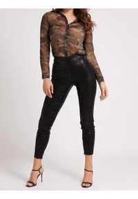 Gennemsigtig, camouflagemusteret langærmet skjorte kombineret med højhalserede, sorte leggings i faux læder og sorte stiletter med remme.