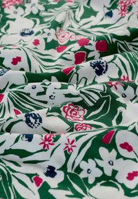 Cotton fabric featuring a floral pattern with green, white, pink, and navy colors; soft texture and draped folds.