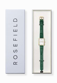 Reloj cuadrado con esfera blanca, accesorios dorados y correa de cuero grabada con piel de cocodrilo verde, presentado en una caja azul clara.