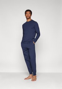 Navy long-sleeve top and matching pants made of soft cotton, featuring a relaxed fit and side pockets; subtle detailing at cuffs and waist.