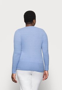 Hellblauer Strickpullover mit strukturiertem Muster, langen Ärmeln und rundem Ausschnitt, kombiniert mit weißen Hosen.