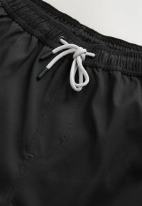 Sorte badetights med elastisk talje, der har en grå snor og en frontlomme med diskrete syningsdetaljer.