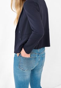 Marynarski, krótki żakiet na dwa guziki, w połączeniu z jasnoniebieskimi dżinsami. Materiał jest gładki i ma swobodny krój.